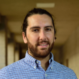 A bearded man with long dark hair pulled back into a bun