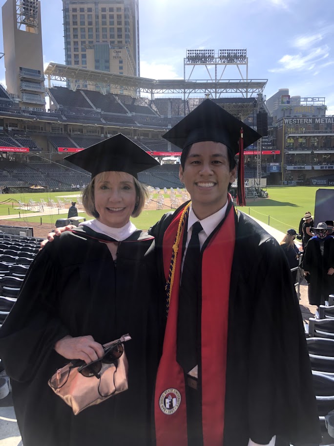 A woman and young man wear graduation regalia at an outdoor stadium