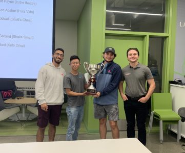 Four male students celebrate winning a competition by holding a trophy